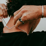 Man putting on a silver necklace while wearing the Abyss Ring with black onyx stone, showcasing minimalist men's jewellery