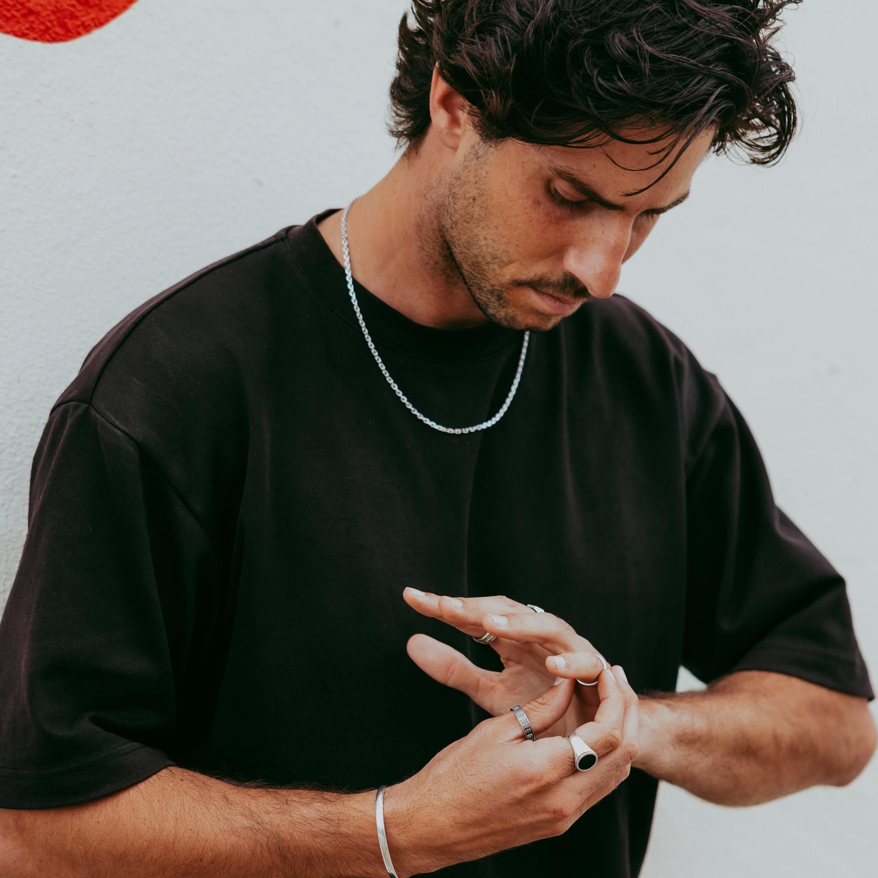 Man adjusting silver rings while wearing the Abyss Ring with black onyx stone, casual street style with minimalist jewellery