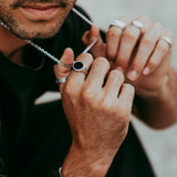 Man wearing the Abyss Ring with black onyx stone while adjusting a silver necklace, showcasing a minimalist jewellery style