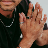 Man showing hands while wearing the Abyss Ring with black onyx stone and multiple silver rings, minimalist jewellery style