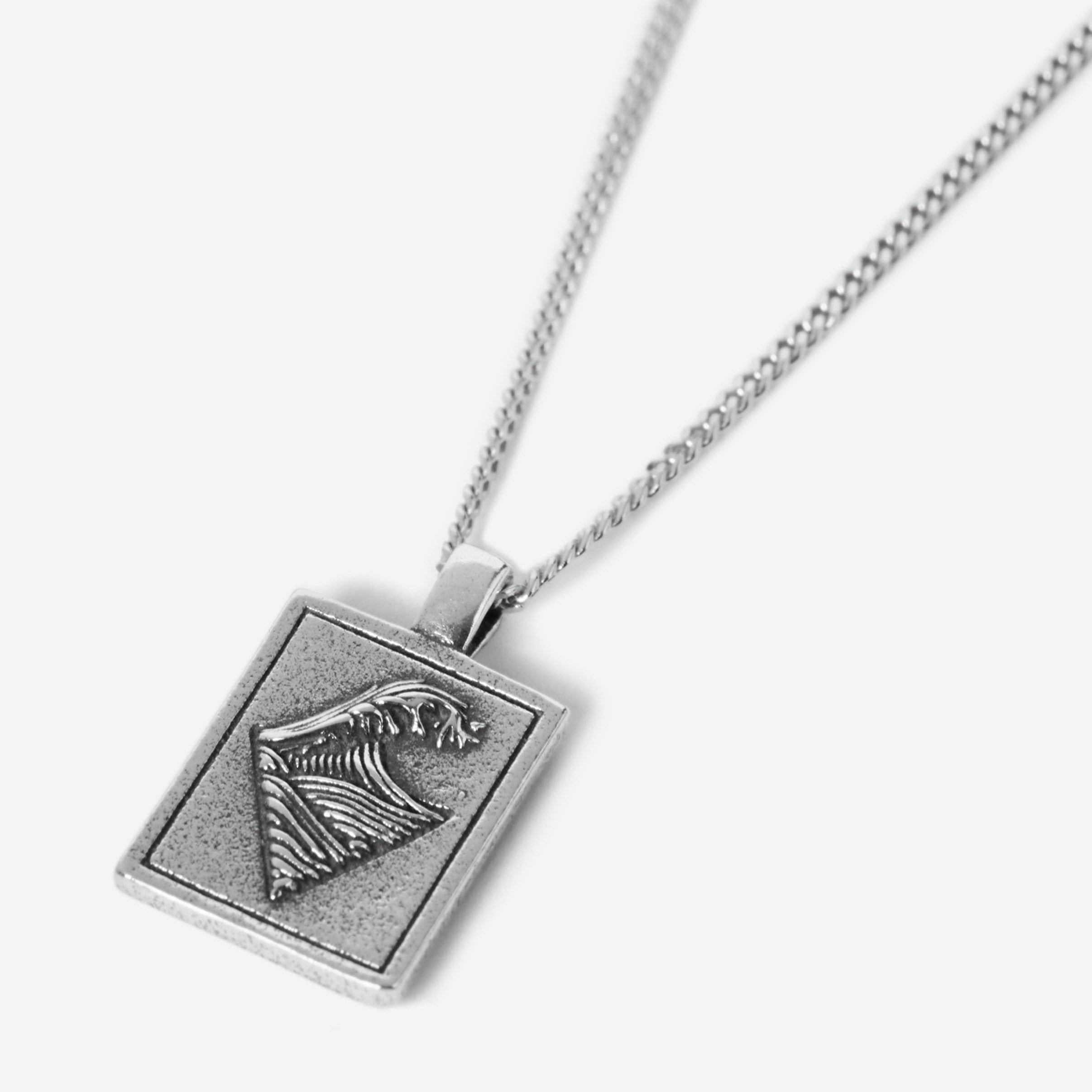 A silver rectangular pendant necklace featuring an engraved ocean wave design, shown against a plain white background.