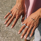 Close-up of a person's hands with tattoos and rings on a textured surface