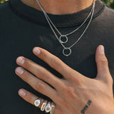 Man wearing a silver necklace with circular snake pendants and multiple rings on a black background
