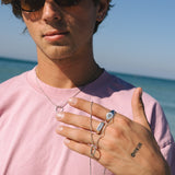 Man wearing sunglasses and a pink shirt with jewelry on a beach