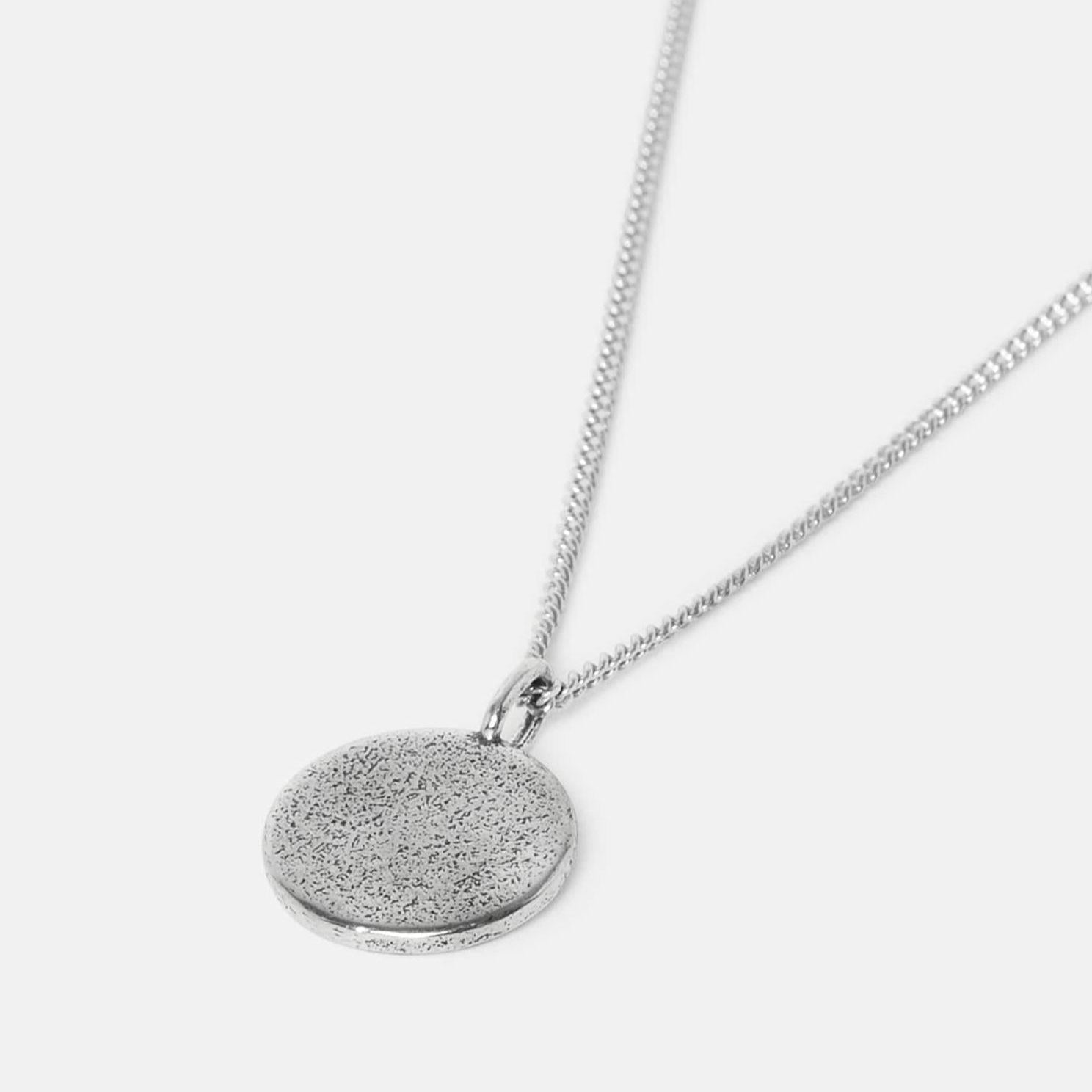A silver chain necklace with a round, textured, flat pendant shown against a plain white background.